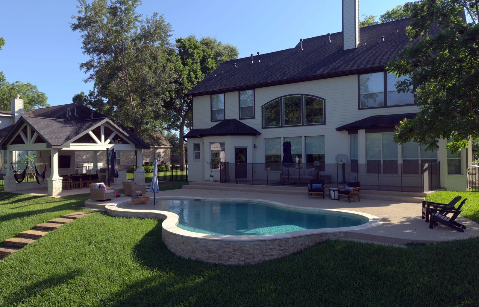Backyard pool with stone wall and covered patio built by Mango Pool & Spa in Fulshear, Texas