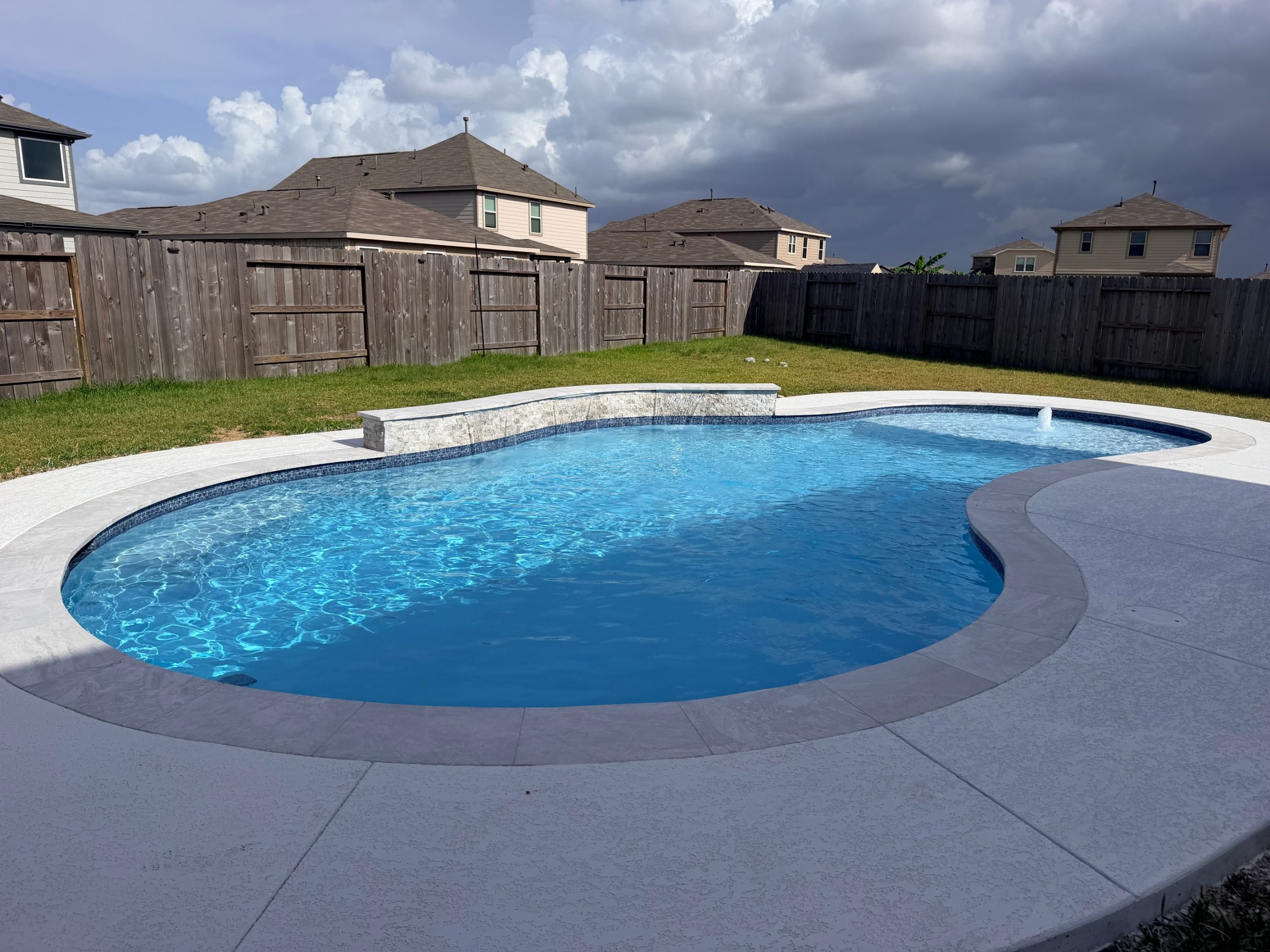 Freeform pool with a stone wall, sheer descent waterfalls and tanning ledge built by Mango Pool & Spa in Katy, Texas