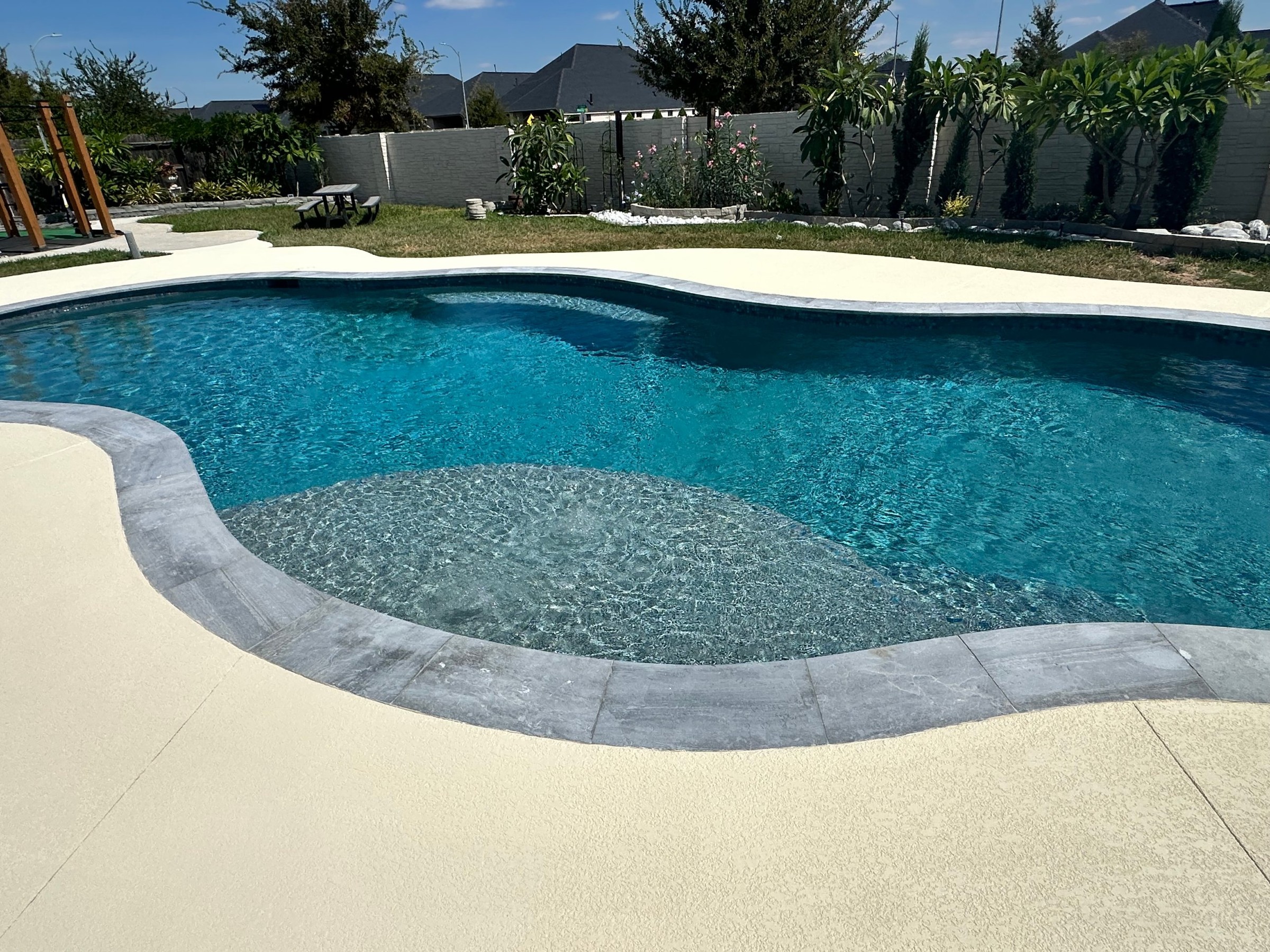 Tanning ledge and gray stone coping on a freeform pool built by Mango Pool & Spa in Katy, Texas