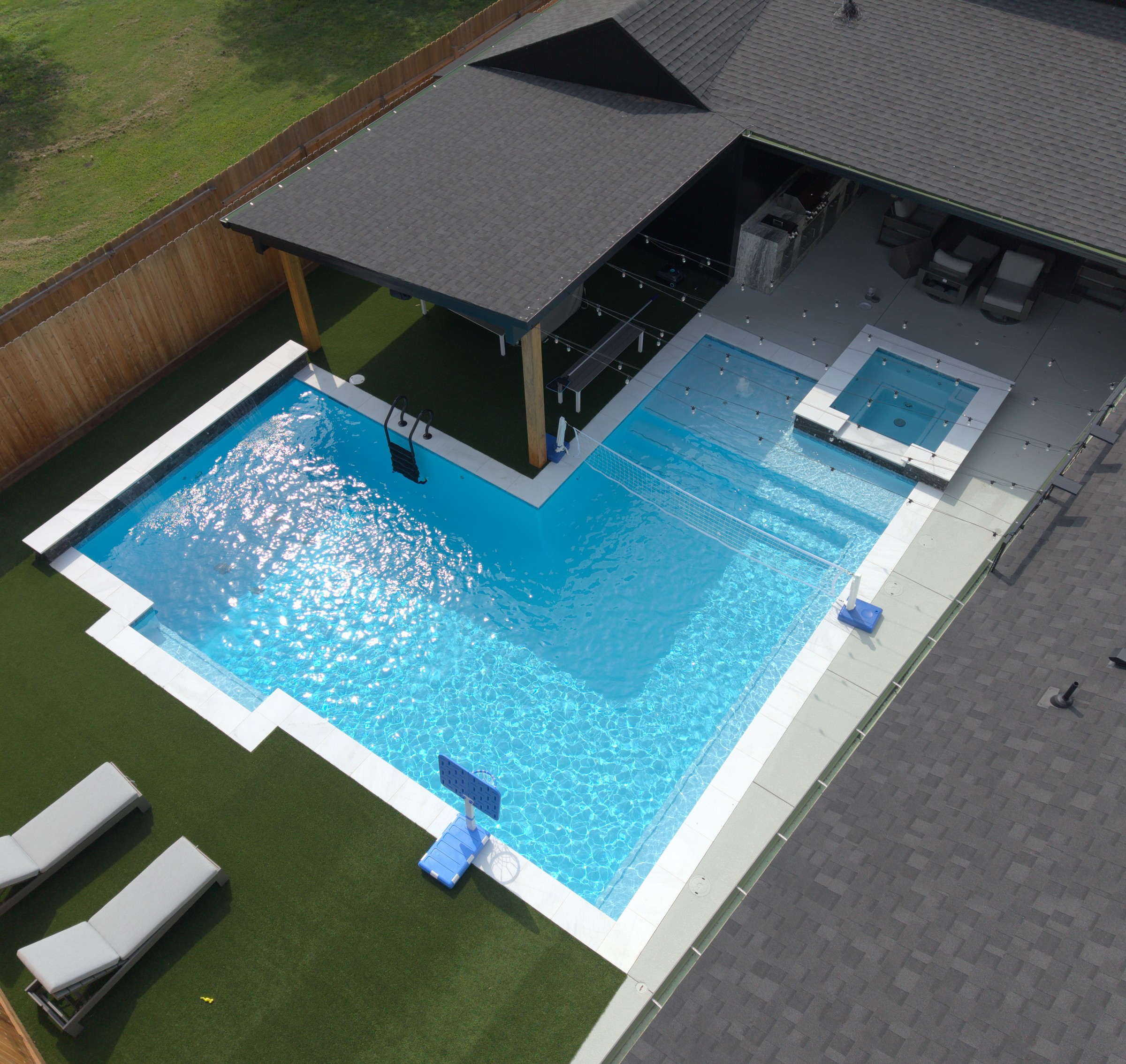 Aerial view of an L-shaped pool with a raised spa, covered patio and outdoor kitchen built by Mango Pool & Spa in Houston, Texas