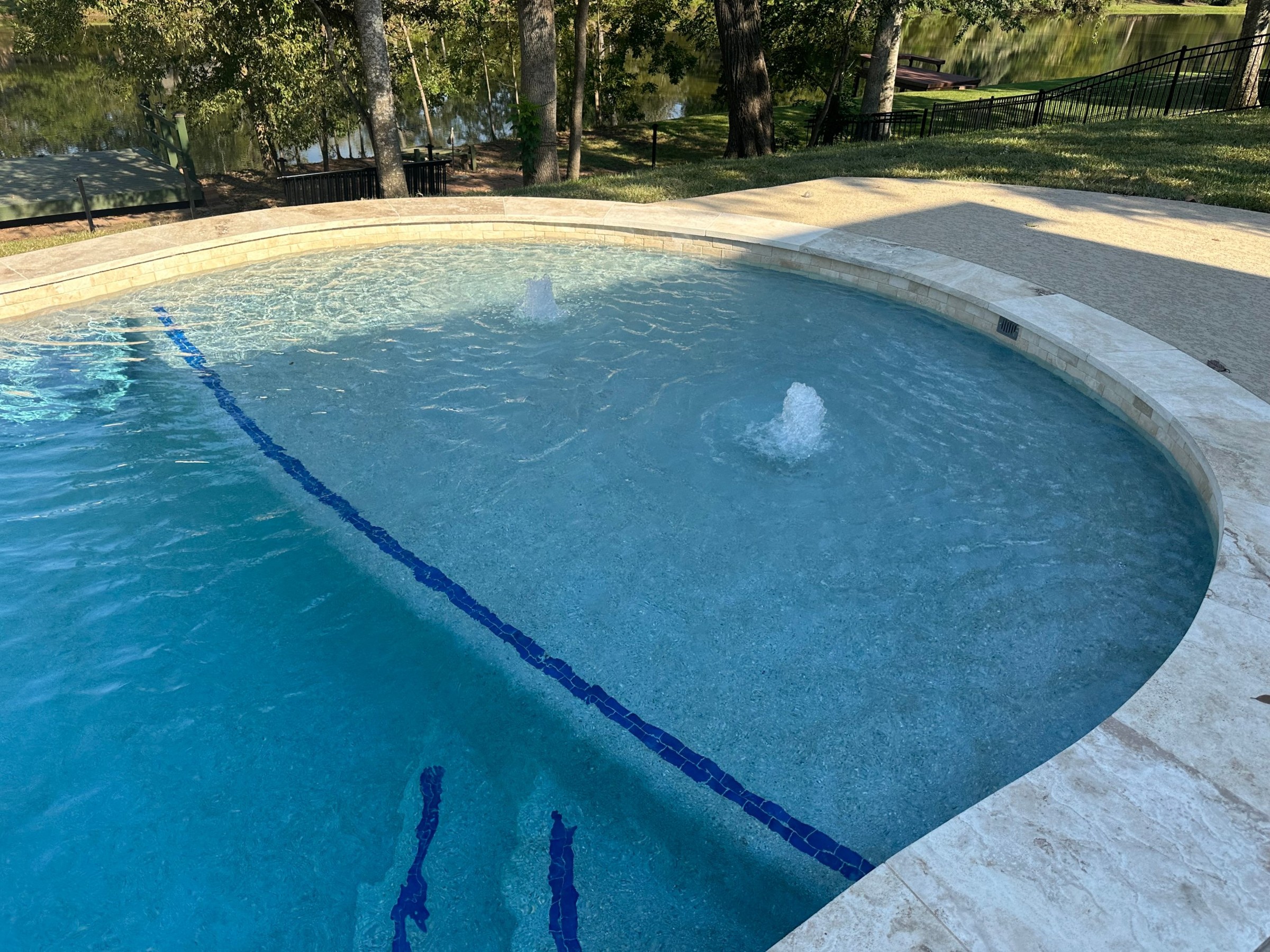Freeform pool with bubblers on a shallow ledge and travertine coping in Fulshear, Texas