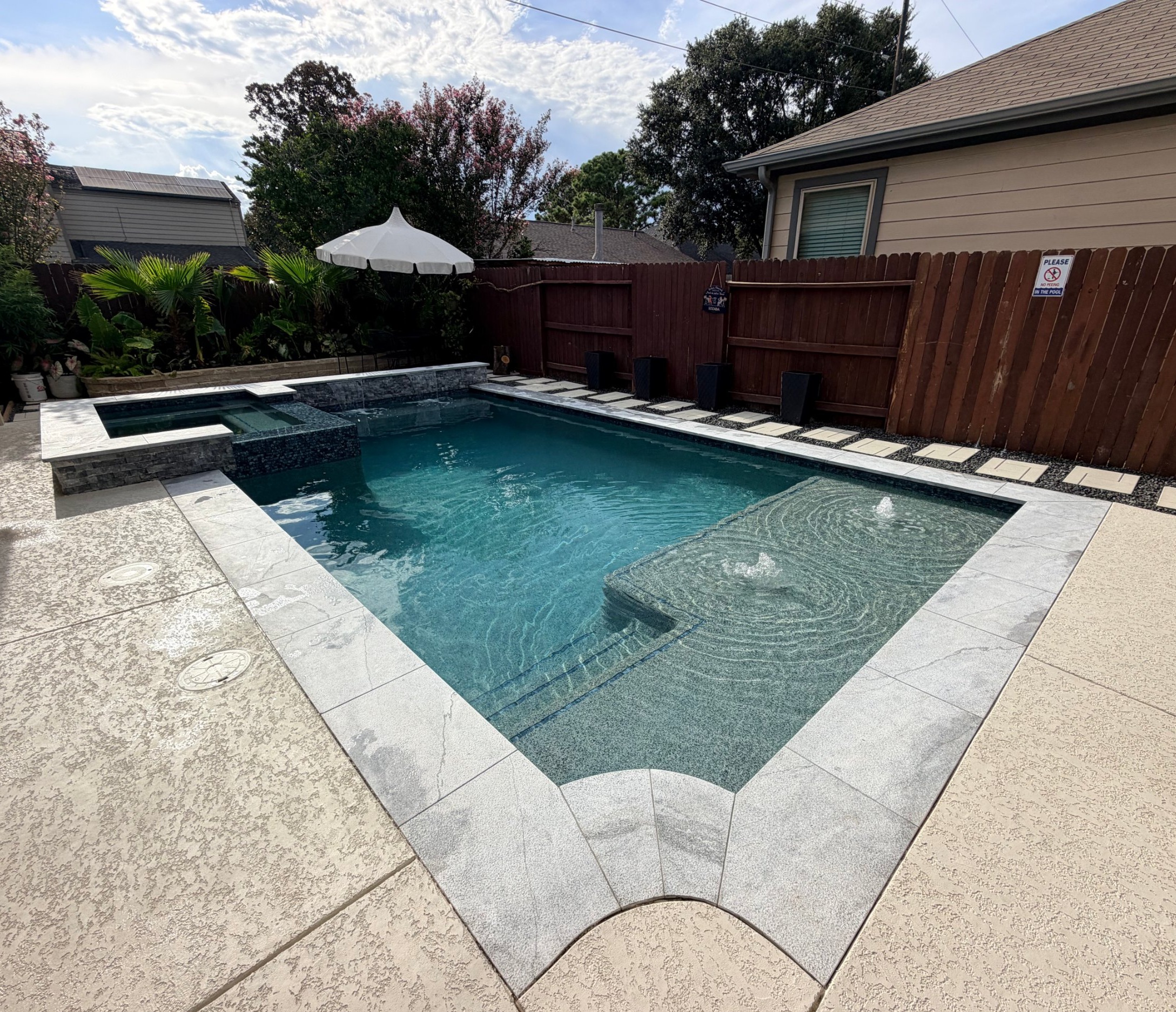 Rectangular pool with a raised spa, gray stone coping and tanning ledge with bubblers built by Mango Pool & Spa in Houston, Texas